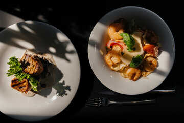 medallions and salad with shrimp on a black background with shadows from the window. Top view