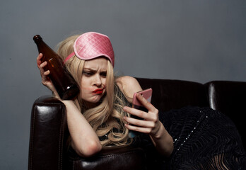 A woman in a pink mask lies on the couch with a bottle of beer and a phone in her hand
