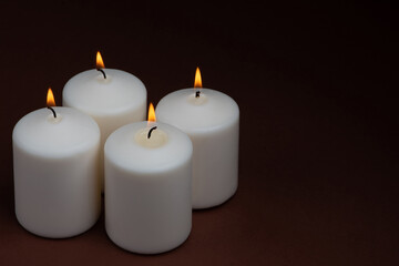 Fototapeta na wymiar Four white candles flame burning on dark background with copy space for text.