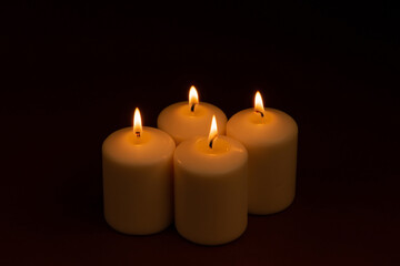 Fototapeta na wymiar Four white candles flame burning on dark background with copy space for text.