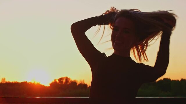 Happy extatic lady in her 30s turning around with her long blond hair flying in the air in slow motion. Sunset summer time.