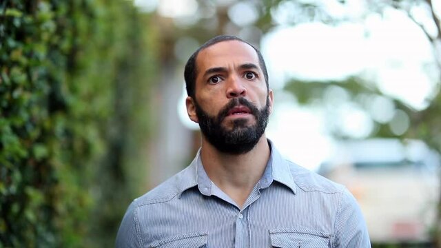 Pensive man walking outside in sidewalk. Thoughtful hispanic guy daydreaming outdoors city walk