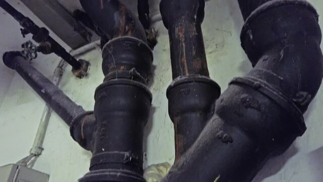 Old sewer pipes mounted on wall with traces of leaks go into the ceiling with destroyed plaster