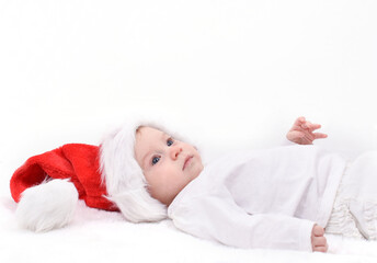 Christmas baby. Cute four month old caucasian baby in a Santa Claus hat lying on back looking up. Copy space. Christmas and New Year card.