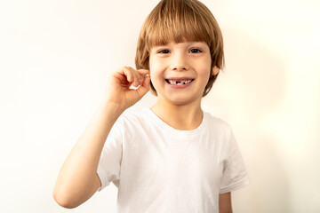 little toothless boy holds a fallen milk tooth in his hand and smiles