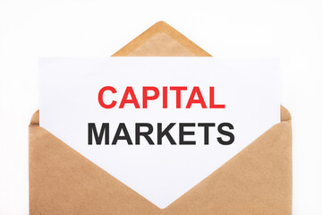 A white sheet with the text capital markets lies in an open craft envelope on a white background with copy space. Business concept image