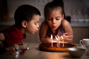 Little children blowing on candles on cake at home