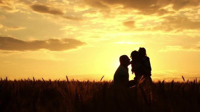 Silhouettes of family in wheat field at sunset in slow motion. Father is throwing up his son in the air. Mother is holding her daughter on arms. Concept of spending time together and weekend on nature