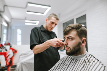 Portrait of a bearded male client sitting in a chair and crouching in a barber, looking away with a serious face. Man with beard and hair care in barbershop. Haircut in a professional barber.