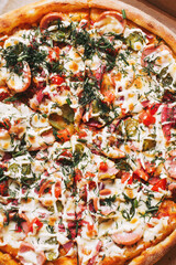 Homemade pizza with sausages, pickled cucumbers, tomatoes and cheese, crispy in a cardboard box for delivery to the client