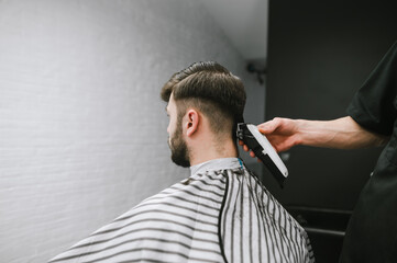 Barber hand with clipper cuts hair on head in bearded adult client on black and white background. Barber shop concept. Creating a stylish hairstyle in a men's hairdresser. Background