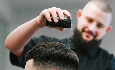Close photo. Positive barber pours white powder for styling on client's hair. Smiling hairdresser...