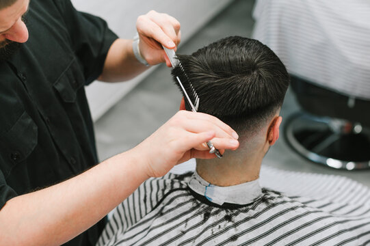 Closeup photo, male hairdresser clipping client's hair with scissors. Barber trims a man in a light barber shop, use scissors. Men's haircut concept.