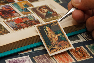 The philatelist holds the postage stamp using tweezers above the stamp album - obrazy, fototapety, plakaty