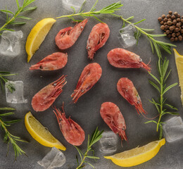 shrimps on a gray stone table with lemons, salt and herbs and ice cubes