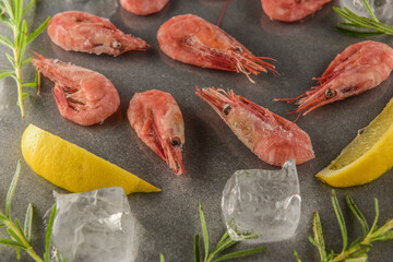 shrimps on a gray stone table with lemons, salt and herbs and ice cubes