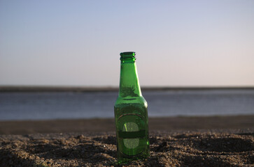 Garrafa verde vazia de vidro de água, refrigerante ou cerveja pousada na areia da praia com...