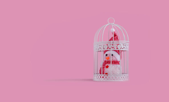 Snowman inside the birdcage on pastel pink background as concept for corona virus pandemic. Flat lay design