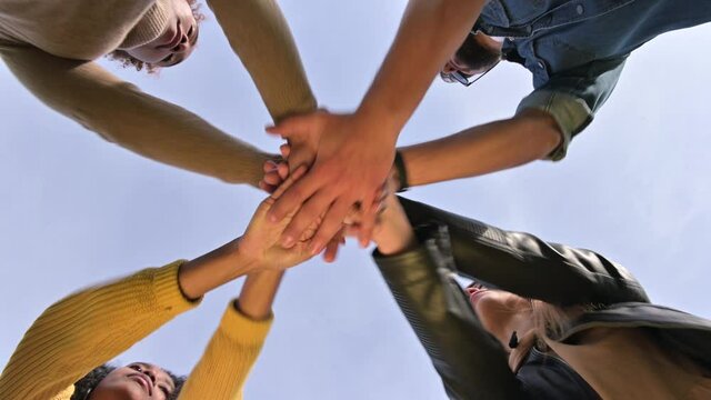 The team puts their hands together and shakes against the sky. Unity of a multinational company