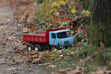 Red and blue toy industrial truck vehicle left behind on the side of a pathway filled with autumn...