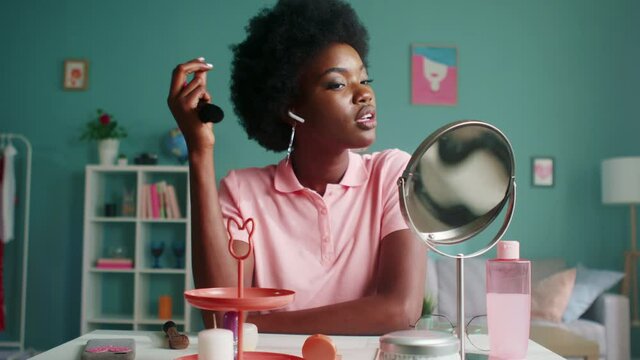 Young black woman is sitting at beauty table at home, getting ready to go outside, smiling at mirror and correcting her hairstyle, Foreground, Slow motion.