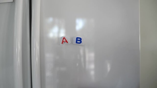 Woman placing alphabet magnets on white fridge spelling ABCDE