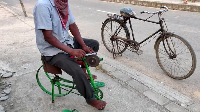 Slow cinematic hands of a man sharpening a knife on a DIY makeshift sharpening machine on a bicycle frame.