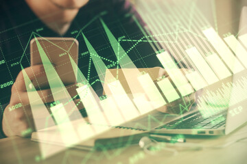 Double exposure of man's hands holding and using a phone and financial graph drawing. Analysis concept.