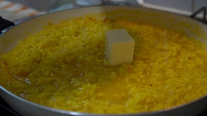 Chef adding butter and freshly grated parmesan cheese to a yellow saffron risotto. - Powered by Adobe