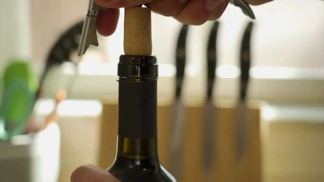 Man's hands pulling a cork out of a wine bottle with a corkscrew