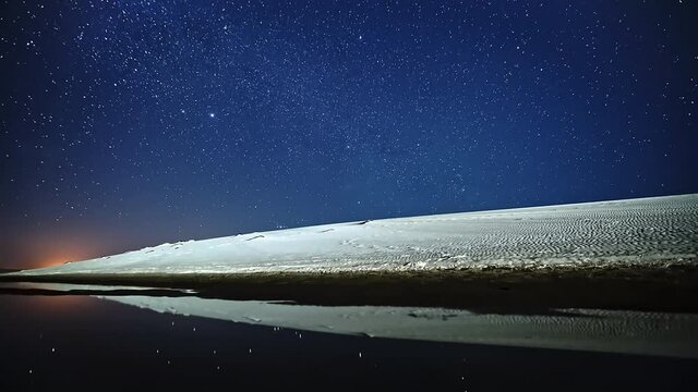 Wonderful time lapse of the stars over sand dunes with the reflex of the stars projected on a lake.