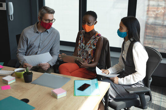 Diverse colleagues wearing face masks laughing together at modern office