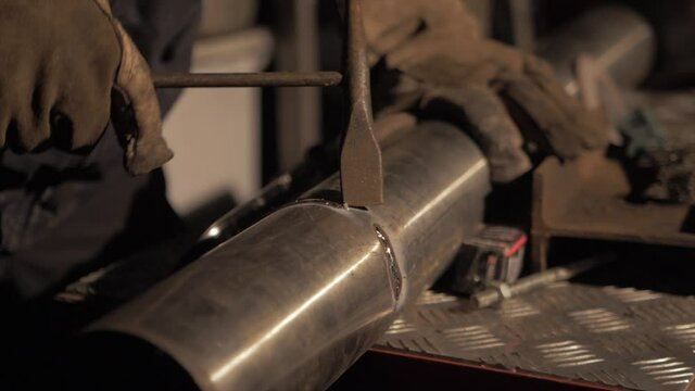 Welder breaking off any excess weld flux with hammer
