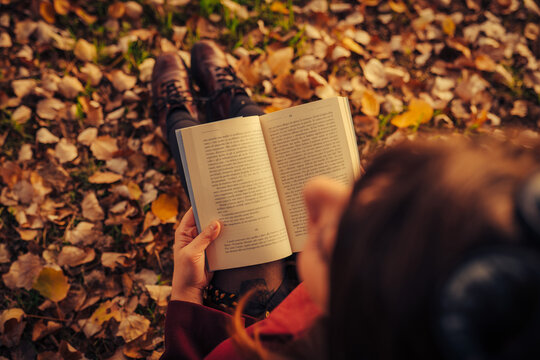 Young Woman With Red Coat Reading A Book Sitting On The Ground In An Autumn Park Surrounded By Yellow Leaves