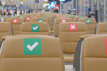 Row of empty seats in the airport with social distancing regulation sign for COVID-19 epidemic awareness. Selective focus.