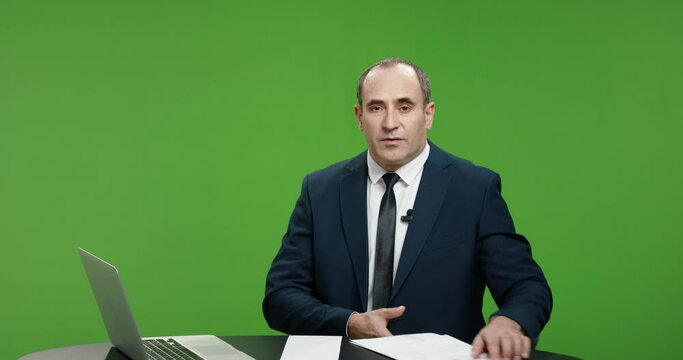 Male television anchor is talking about current news. Serious professional tv channel broadcast news reporter looking at camera. Green background chroma key template 4k footage