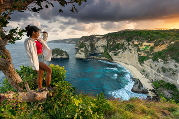 A travel girl with backpack and in shorts on the ocean, cliffs and Diamond Beach – Most Beautiful Beach on Nusa Penida in Bali. Indonesia.
