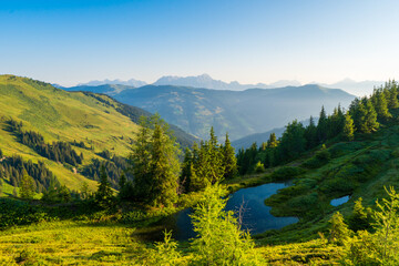 Idyllic landscape with mountain top above green pastures under a blue sky with white clouds high up...