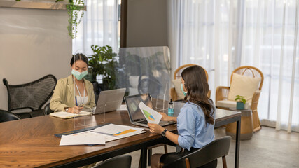 Female business workers with  face mask having business discussion or agreement through transparent...