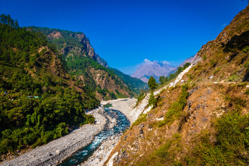 Fototapeta na wymiar View of Ramganga river and the valley to the fields on the background of blue sky and mountain ranges of the Himalayas, near Nainital, Uttarakhand, India.