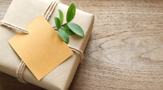 empty card on gift box wrapped in recycled paper with rope and leaf on wood background with copy space for text or image / green concept
