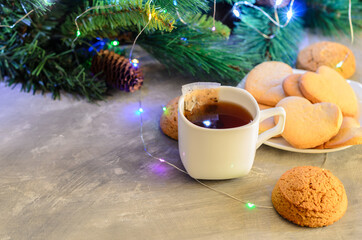 Homemade cookies in the shape of a heart in a white plate with a mug and a tea bag on the background of Christmas decorations.