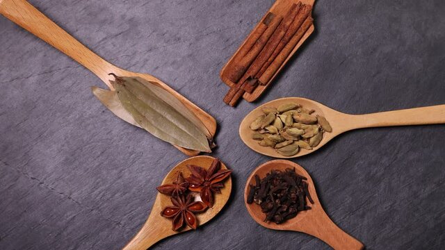 Mix variety spice cinnamon cardamom clove bay leaf wooden spoon dropping on black slate background