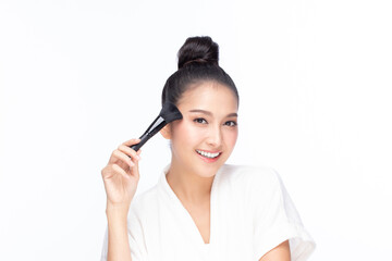 Obraz premium Closeup portrait of beautiful happy young girl holding brush near face isolated on white background. Beauty and cosmetics concept.