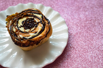 Cinnamon rolls with various sweet toppings and chocolate on a white plate on the pink glitter background.