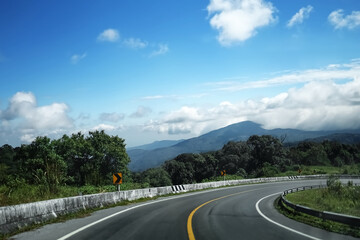 The steep curve descending from the mountain top overlooking the sky and white clouds, and on...