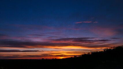 Amazing sunrise in rural scene. Dramatic sky with sunbeam and stratus clouds over the silhouette of hill on the horizon.