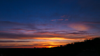 Amazing sunrise in rural scene. Dramatic sky with sunbeam and stratus clouds over the silhouette of hill on the horizon.