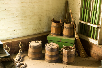 Wooden buckets and broom resting in a corner of a dirty brick building with a wood floor