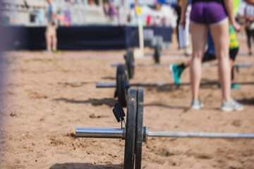 Process of group outdoor training  street workout on a summer sandy beach, with young muscular fit people exercising and lifting heavy weights, making cardio exercise, men and women working out